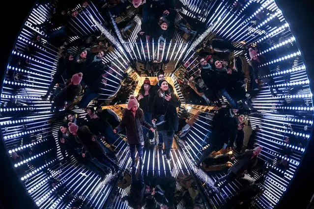 People stand in a giant kaleidoscope, an installation by French artist Guillaume Marmin, during the Festival of Lights (Fete des Lumieres), in Lyon, central eastern France, on December 7, 2023. The Festival of Lights (Fete des Lumieres) is marked each year on December 8, since 1852, on the Feast of the Immaculate Conception, after the city was spared by the plague of 1643. (Photo by Olivier Chassignole/AFP Photo)