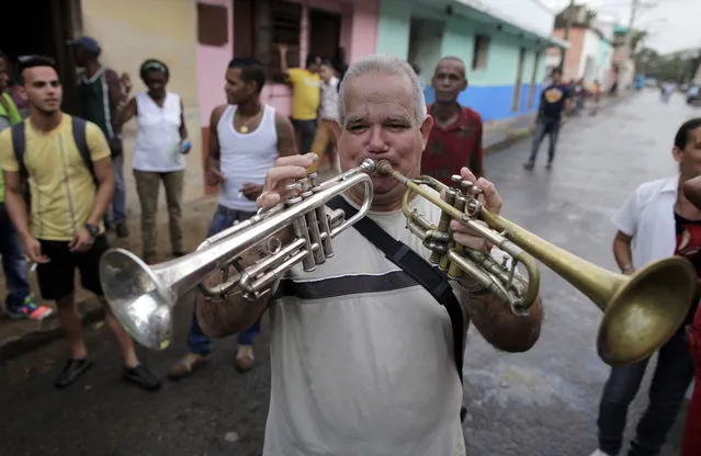 In this February 5, 2014 photo, Carlos Pineiro plays two trumpets during the celebration of a mock funeral known as the Burial of Pachencho in Santiago de Las Vegas, Cuba. (Photo by Franklin Reyes/AP Photo)
