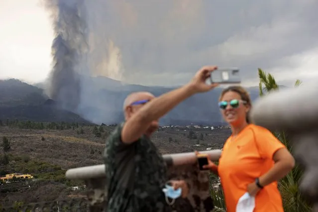 A couple take selfies in front of the eruption of a volcano near El Paso on the island of La Palma in the Canaries, Spain, Monday, September 20, 2021. Lava continues to flow slowly from a volcano that erupted in Spain's Canary Islands off northwest Africa. Officials say they are not expecting any other eruption and no lives are currently in danger. (Photo by Gerardo Ojeda/AP Photo)