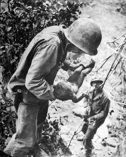 An American Marine lifts a nearly dead infant from a cave where native islanders had been hiding during the battle for Saipan between US and occupying Japanese forces while a second Marine watches from below, Saipan, Northern Mariana Islands, July 1944. (Photo by W. Eugene Smith/The LIFE Picture Collection/Getty Images)