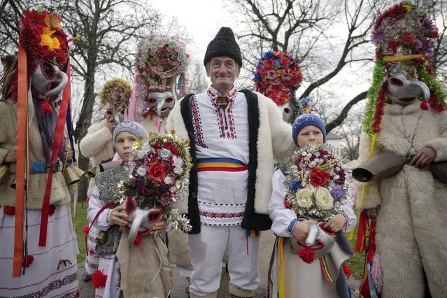 People wearing masks and costumes wait before performing in a show of winter traditions at the Village Museum in Bucharest, Romania, Sunday, December 12, 2021. In pre-Christian rural traditions, dancers wearing colored costumes or animal furs, toured from house to house in villages singing and dancing to ward off evil. (Photo by Vadim Ghirda/AP Photo)