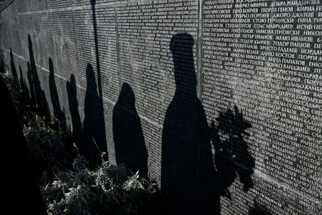 This photograph taken on February 1, 2024, shows shadows of people on a monument listing victims of the communist regime in Bulgaria as they attend an open air mass in Sofia. Bulgaria held commemorations for the victims of the country's 45-year communist regime at the anniversary of the first killings on February 1, 1945. Between December 1944 and April 1945, the self-proclaimed People's Court set up by the newly established communist regime ordered the killing of 2,730 Bulgarians. (Photo by Nikolay Doychinov/AFP Photo)