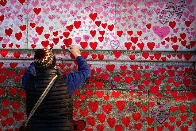 A man writes on a heart at the National Covid Memorial Wall, in Westminster, London on Thursday, January 13, 2022. (Photo by Victoria Jones/PA Images via Getty Images)