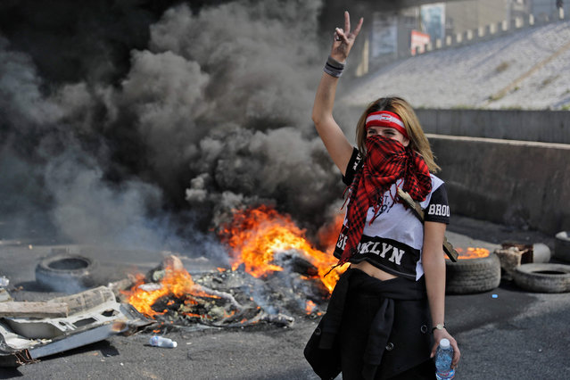A bandana-clad anti-government demonstrator gestures as she stands by the smoke of burning tires at a make-shift roadblock in Zouk Mosbeh north of Lebanon's capital Beirut, on March 8, 2021 during a protest against the deteriorating value of the local currency and dire economic and social conditions. (Photo by Joseph Eid/AFP Photo)
