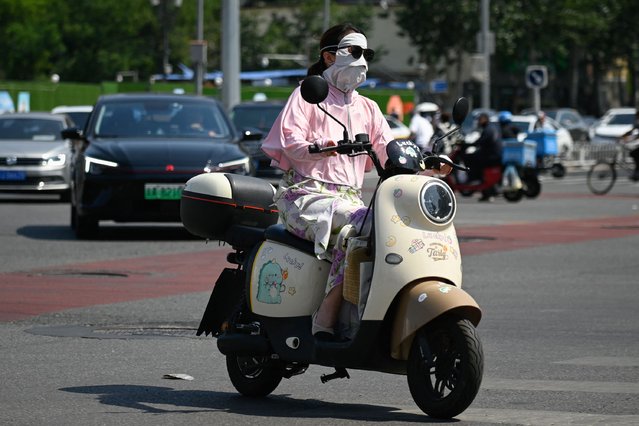 A woman wearing a sun protection mask rides a motorcycle along a road on a hot day in Beijing on June 18, 2024. (Photo by Wang Zhao/AFP Photo)