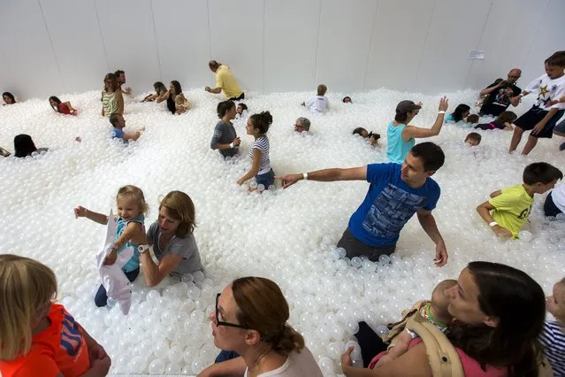 Visitors to an exhibit called “The BEACH” play in  a simulated ocean of nearly one million translucent plastic balls at the National Building Museum in Washington, DC, USA, 11 July 2015. The 10,000 square foot (3,000 square meter) exhibit also includes beach chairs, umbrellas, and a simulated shoreline. (Photo by Jim Lo Scalzo/EPA)