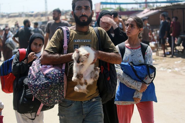 A Palestinian man carries a cat as he flees with others a makeshift camp for displaced people in Khan Yunis in the southern Gaza Strip after Israeli tanks took position on a hill overlooking the area on August 18, 2024, amid the ongoing conflict between Israel and the Hamas militant group. (Photo by Bashar Taleb/AFP Photo)