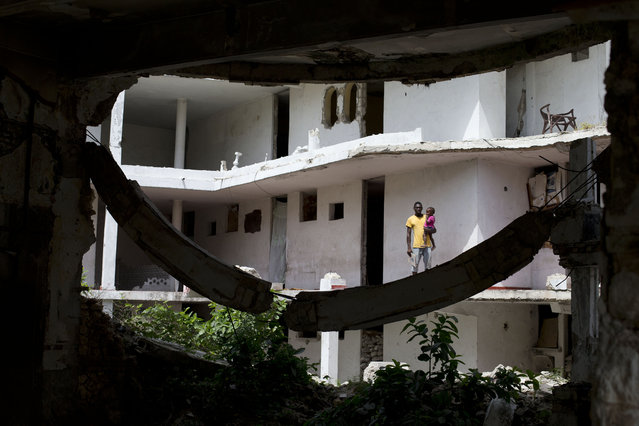 In this June 29, 2015 photo, single father Jean Donalson Tousena Bagui holds his two-year-old daughter outside their room at the earthquake-damaged Hotel Le Palace in central Port-au-Prince, Haiti. Tousena Bagui said he was a security guard at the hotel before the 2010 earthquake and stayed on as a self-appointed caretaker. He receives no compensation, he said, and has not received word from the hotel's owner on what will become of the site. (Photo by Rebecca Blackwell/AP Photo)