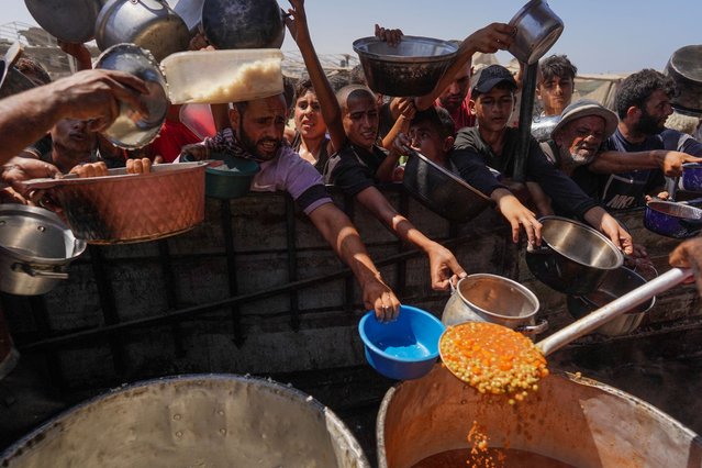 Palestinians receive cooked food rations as part of a volunteer initiative in a makeshift displacement camp in Mawasi Khan Yunis in the besieged Gaza Strip on September 3, 2024, amid the ongoing war between Israel and the Palestinian Hamas movement. (Photo by Bashar Taleb/AFP Photo)