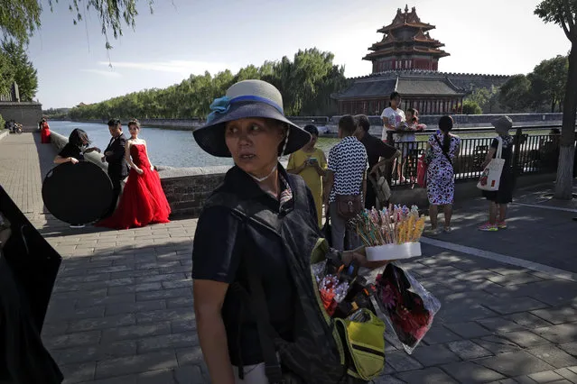 A vendor sells souvenirs as tourists gather near a bride and groom posing for their pre-wedding photos in front of the Turret of the Forbidden City in Beijing, Thursday, August 24, 2017. The Forbidden City, once the isolated palace of China's Ming and Qing Dynasty emperors and now turn into a major tourist attraction, located in the centre of capital city. (Photo by Andy Wong/AP Photo)