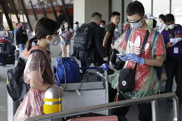 Foreigners wear raincoats before entering departure area of Manila's International Airport, Philippines on Wednesday, March 18, 2020. The Philippine government lifted a 72-hour deadline for thousands of foreign travelers to leave the country's main northern region which has been placed under quarantine due to the growing number of coronavirus infections, officials said. (Photo by Joeal Calupitan/AP Photo)