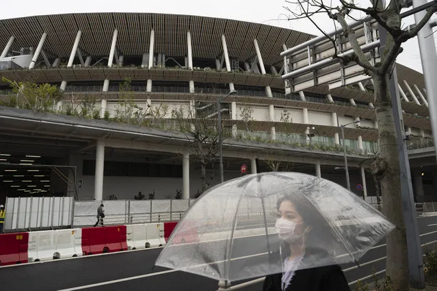 A woman walks past the New National Stadium, a venue for the opening and closing ceremonies at the Tokyo 2020 Olympics, in Tokyo, Monday, March 23, 2020. The IOC will take up to four weeks to consider postponing the Tokyo Olympics amid mounting criticism of its handling of the coronavirus crisis that now includes a call for delay from the leader of track and field, the biggest sport at the games. (Photo by Jae C. Hong/AP Photo)