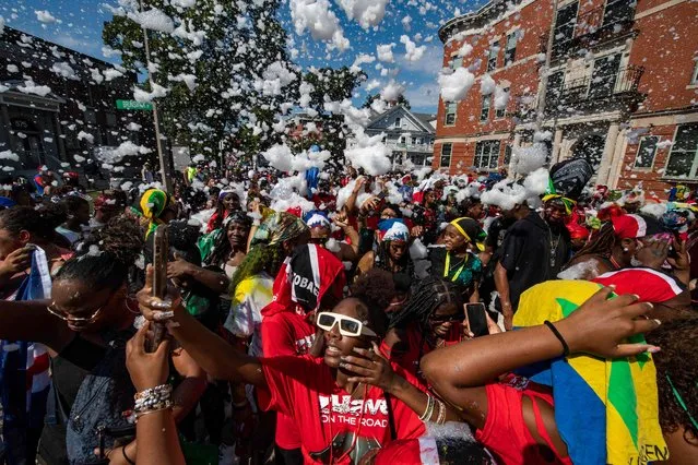 People march and dance as foam is sprayed over them during the 49th Annual Boston Carnival Parade in Boston, Massachusetts on August 27, 2022. The Caribbean American Carnival Association of Boston announced the return of the event after a two-year hiatus due to the Covid-19 pandemic. (Photo by Joseph Prezioso/AFP Photo)