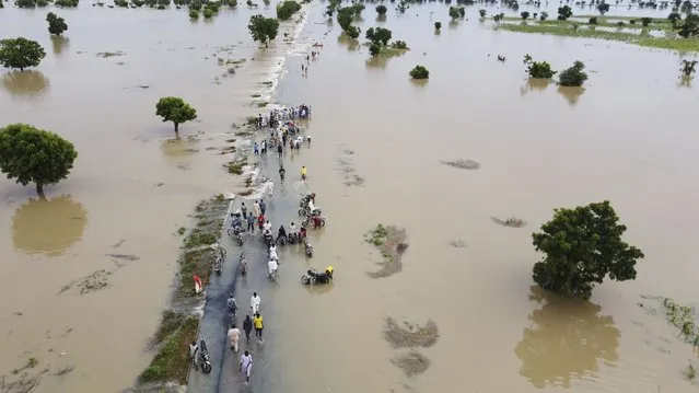 People walk through floodwaters after heavy rainfall in Hadeja, Nigeria, Monday, September19, 2022. Nigeria is battling its worst floods in a decade with more than 300 people killed in 2021 including at least 20 this week, authorities told the Associated Press on Monday. (Photo by AP Photo/Stringer)