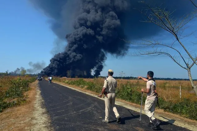 Policemen gesture as they ask people to move to a safer place as smoke rises to the sky following an explosion at an oil well operated by the state owned Oil India Limited (OIL) in Baghjan, Tinsukia district in the northeast Indian state of Assam on June 9, 2020. (Photo by Partha Sarathi Das/AFP Photo)