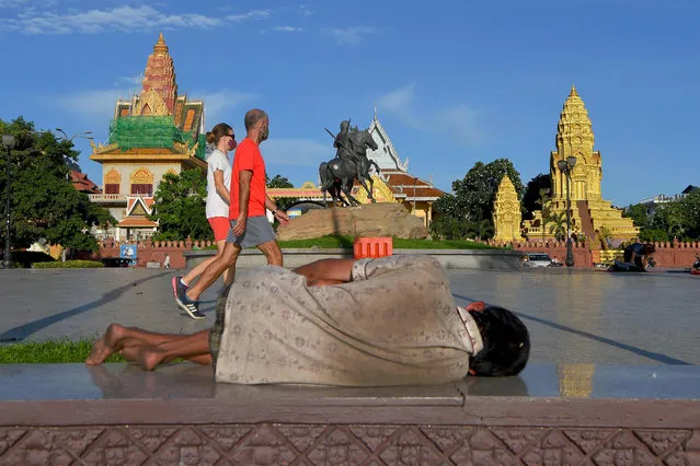A homeless man lays on the floor as a couple wearing face masks walk past in Phnom Penh on June 23, 2020, as sectors of the economy are being reopened following restrictions to halt the spread of the COVID-19 coronavirus. (Photo by Tang Chhin Sothy/AFP Photo)