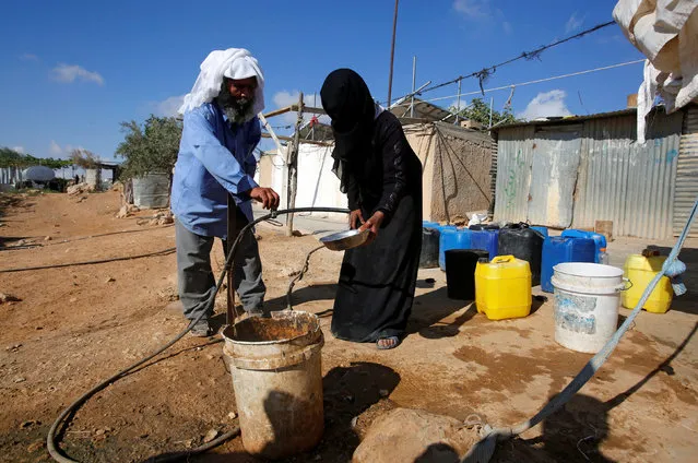 A Palestinian man washes a dish for a woman near their houses on the outskirts of the West Bank village of Yatta, south of Hebron, August 17, 2016. (Photo by Mussa Qawasma/Reuters)