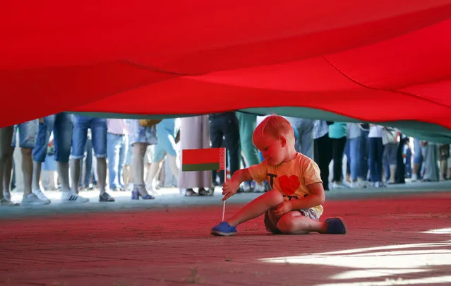A boy plays sitting under a huge Belarusian State flag during a pro-government rally of Belarusian President Alexander Lukashenko's supporters in the Brest Fortress memorial, in Brest, 360 kilometers (225 miles) southwest of Minsk, Belarus, Friday, August 21, 2020. (Photo by Dmitri Lovetsky/AP Photo)