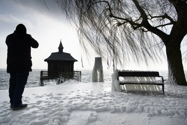 A man taking pictures of  an ice-covered bench, on the frozen shores of the Lake of Neuchatel, in Gorgier, Switzerland, Wednesday, February 28, 2018. A cold spell has reached central and eastern Europe with temperatures far below the freezing point. (Photo by Laurent Gillieron/Keystone via AP Photo)