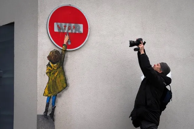 A man takes a picture of an artwork of the famous street artist TvBoy in the town center of Bucha, outside Kyiv, Ukraine Monday, January 30, 2023. (Photo by Efrem Lukatsky/AP Photo)