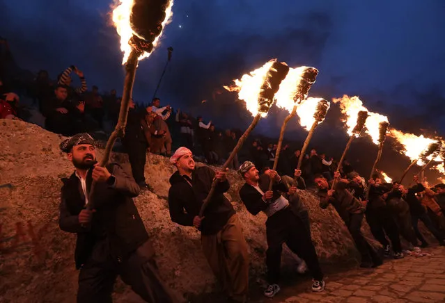 Iraqi Kurds holding lit torches walk up a mountain during a procession to celebrate their Nowruz New Year festival in Akre, the country's northern autonomous Kurdish region, on March 20, 2023. Millions of people across the Middle East, Asia and Eastern Europe celebrate Nowruz new year festival, which marks the start of spring. (Photo by Safin Hamed/AFP Phoot)