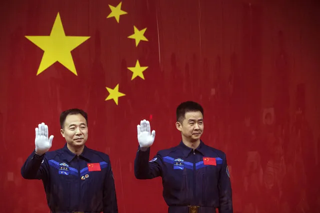 Chinese astronauts Jing Haipeng, left, and Chen Dong, right, wave from behind a glass enclosure during a presser at the Jiuquan Satellite Launch Center in northwest China Sunday October 16, 2016. Chinese officials unveiled plans for Monday's launch of the country's latest space mission in which the two astronauts will be blasted into space and will dock with an orbiting space lab. (Photo by Chinatopix via AP Photo)