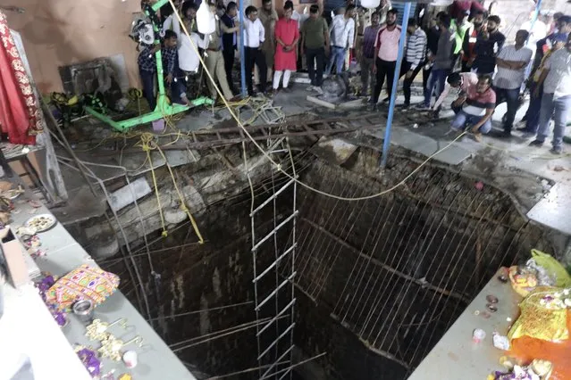 People stand around a structure built over an old temple well that collapsed Thursday as a large crowd of devotees gathered for the Ram Navami Hindu festival in Indore, India, Thursday, March 30, 2023. Up to 35 people fell into the well in the temple complex when the structure collapsed and were covered by falling debris, police Commissioner Makrand Deoskar said. At least eight were killed. (Photo by AP Photo/Stringer)