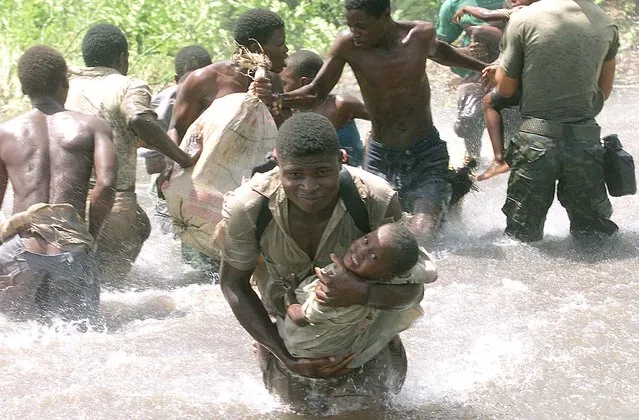 A Mozambican soldier runs with a child through flood water towards a helicopter in the central district of Cocorico March 2, 2001. (Photo by Juda Ngwenya/Reuters)