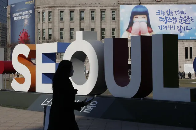 A woman wearing a face mask as a precaution against the coronavirus walks near the display of South Korea's capital Seoul logo in Seoul, South Korea, Monday, December 21, 2020. (Photo by Lee Jin-man/AP Photo)
