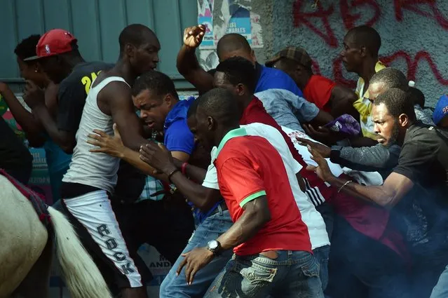 Presidential candidate Steven Benoit(C blue shirt) and supporters of the LAPEH, Fanmi Lavalas and Petit Dessalines political parties run from tear gas fired by Haitian police during protests against the results given by the Provisional Electoral Council (CEP), the Haitian President Michel Martelly, and against the candidate of the ruling party Jovenel Moise, in the commune of Petion Ville, in Port-au-Prince, on November 18, 2015. (Photo by Hector Retamal/AFP Photo)