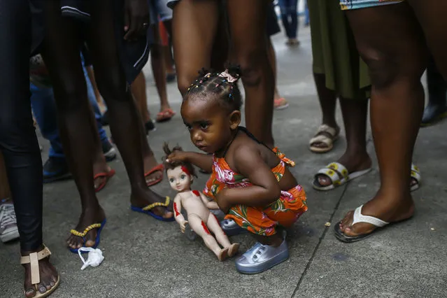 Kimberly, 1, holding a doll with fake blood, is seen during a protest against the killing of her cousins Emily Victoria Silva dos Santos, 4, and Rebeca Beatriz Rodrigues dos Santos, 7, in Duque de Caxias, Rio de Janeiro state, Brazil, Sunday, December 6, 2020. The girls, cousins, were killed by stray bullets while playing outside their homes. (Photo by Bruna Prado/AP Photo)