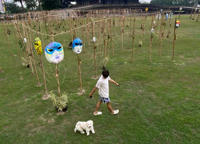 A person and a dog walk near an art installation of masks on Bamboo poles during Earth Day in Manila, Philippines, 22 April 2023. Earth Day is an annual event celebrated on April 22nd worldwide. (Photo by Francis R. Malasig/EPA)