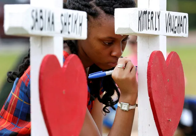 Jai Gillard, a freshman at Santa Fe High School, writes a message on a cross at a makeshift memorial left in memory of the victims killed in a shooting in Santa Fe, Texas, U.S., May 21, 2018. (Photo by Jonathan Bachman/Reuters)