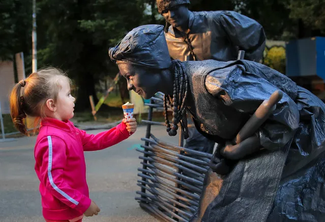 In this Thursday, May 24, 2018, photograph, a child offers ice-cream to artists of Ukraine's Artel Myth theatre performing “A day in the life of Ukrainians” at the Living Statues International Festival, in Bucharest, Romania. (Photo by Vadim Ghirda/AP Photo)