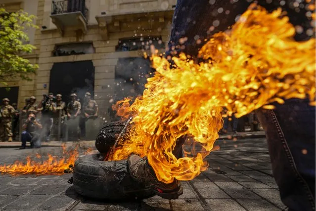 A protesting depositor kicks a burning tire as Lebanese soldiers, background, stand guard in front of the Banking Association during a protest in Beirut, Lebanon, Tuesday, May 9, 2023. Depositors for years have protested at the banks, demanding their trapped savings bank, as they struggle from an economic crisis that has plunged over three-quarters of the tiny country's population into poverty. Lebanese banks since late 2019 have enforced formal capital controls due to currency shortages, severely restricting people's savings. Lebanon has yet to enforce financial reforms that would restructure the banks and its battered economy. (Photo by Hassan Ammar/AP Photo)
