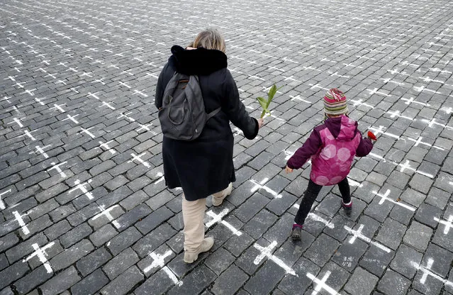 A woman and a small child carry flowers as thousands of crosses are painted at the Old Town Square, to commemorate the 1-year anniversary of the death of first Czech COVID-19 patient, in Prague, Czech Republic, Monday, March 22, 2021. Bells were tolling all across the Czech Republic at Monday noon to honor those who have died of COVID-19 in one of the hardest-hit European Union countries. A 95-year-old man was the first to pass away on March 22, 2020 at Prague's Bulovka hospital. (Photo by Petr David Josek/AP Photo)