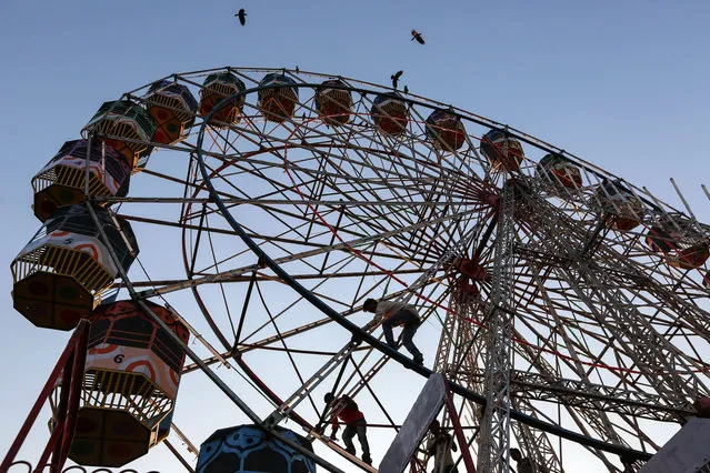 People work on a ferris wheel in an amusement park during the annual Mahim Fair in Mumbai, India, 29 December 2015. The ten-day fair features giant wheels, toy trains and gravity-defying stunts in the “Maut Ka Kuan” or “Well of Death” in honor of the Sufi saint Makhdoom Ali Mahimi. (Photo by Divyakant Solanki/EPA)
