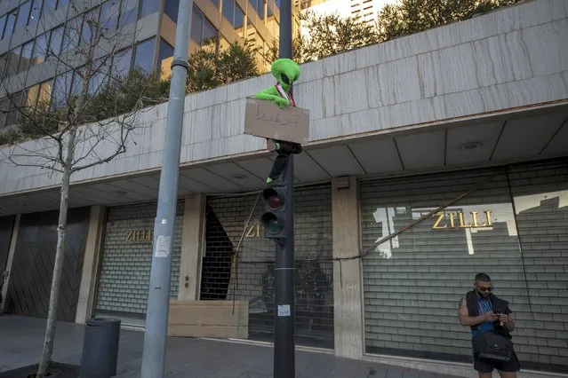 An anti-government protester stands on a traffic light as holds a placard that reads in Arabic "Unite" during a protest against the rising prices and worsening economic and financial conditions, in Beirut, Lebanon, Friday, March 12, 2021. Lebanon’s parliament on Friday approved a $246 million loan from the World Bank that would provide cash assistance for more than 160,000 families in the small country hit by an unprecedented economic crisis and the coronavirus pandemic. (Photo by Hassan Ammar/AP Photo)