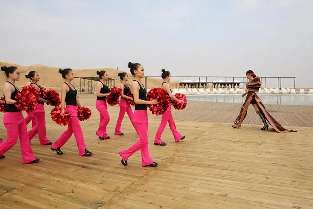 A model in Mongolia costumes walks past the dancers in Xiangshawan Desert, also called Sounding Sand Desert on July 18, 2013 in Ordos of Inner Mongolia Autonomous Region, China. Xiangshawan is China's famous tourist resort in the desert. It is located along the middle section of Kubuqi Desert on the south tip of Dalate League under Ordos City. Sliding down from the 110-metre-high, 45-degree sand hill, running a course of 200 metres, the sands produce the sound of automobile engines, a natural phenomenon that nobody can explain. (Photo by Feng Li/Getty Images)