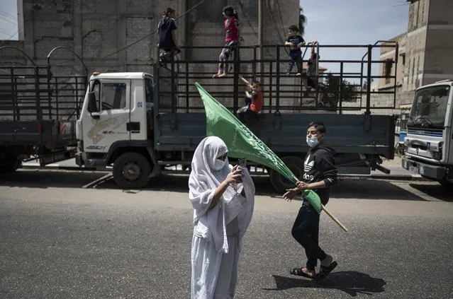 Palestinian children swing on the back of a truck as a young girl uses a mobile phone to photograph Hamas supporters protest in solidarity with Muslim worshippers in Jerusalem, in Gaza City, Friday, April. 23, 2021. (Photo by Khalil Hamra/AP Photo)