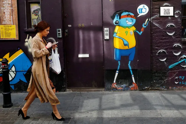 A woman looks at her mobile phone as she passes a mural in Shoreditch, London, Britain October 5, 2016. (Photo by Stefan Wermuth/Reuters)