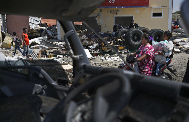 Motorists ride past a destroyed vehicle at the earthquake-affected area in Palu, Central Sulawesi, Indonesia, Wednesday, October 3, 2018. Aid has yet to reach the hardest-hit areas around Palu, the largest city heavily damaged in the earthquake and tsunami that hit on Friday, Sept. 28. (Photo by Dita Alangkara/AP Photo)