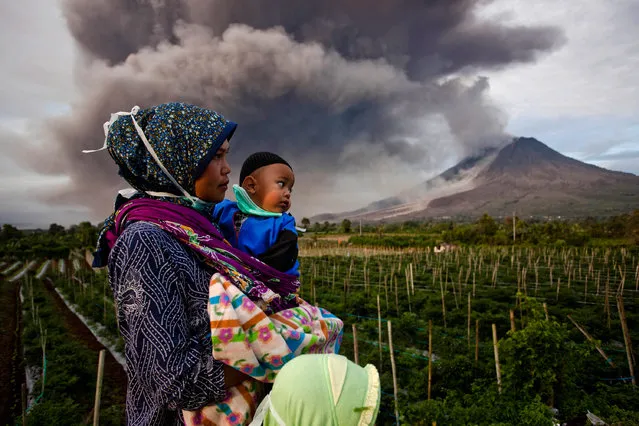 A woman carries her son as they watch Mount Sinabung spew pyroclastic smoke on January 8, 2014 in Karo District, North Sumatra, Indonesia. (Photo by Ulet Ifansasti/Getty Images)