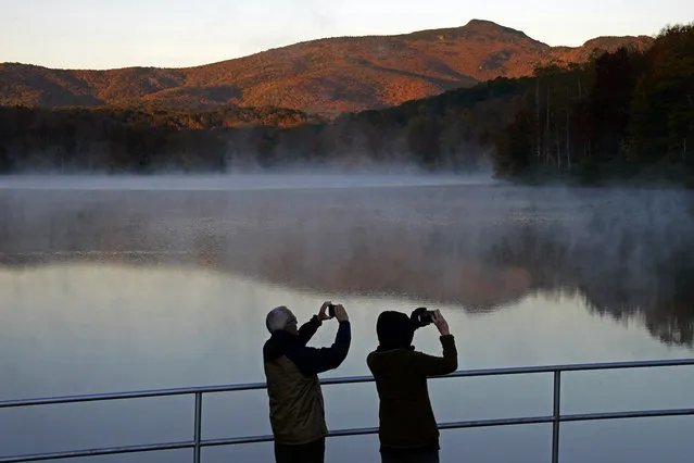 A couple takes photos as the sun rises at Price Lake along the Blue Ridge Parkway near Blowing Rock, N.C., Tuesday, October 19, 2021. (Photo by Gerry Broome/AP Photo)