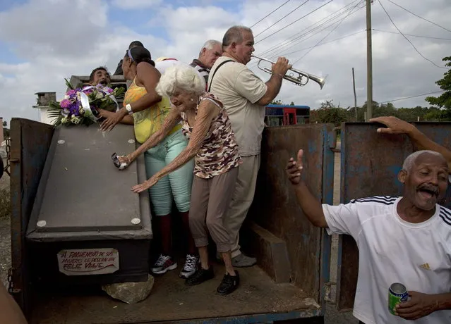 In this February 5, 2014 photo, Divaldo Aguiar, who plays the part of Pachencho, left, lies inside a coffin as Carmen Zamora, who plays his widow, center, stands near the coffin, during the town's annual tradition, known as the Burial of Pachencho, at a cemetery in Santiago de Las Vegas, Cuba. (Photo by Enric Marti/AP Photo)