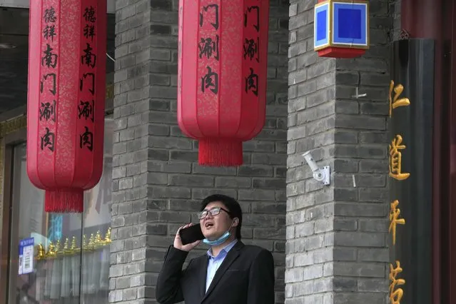 A man lowers his mask to speak on his phone outside a restaurant in Beijing, China, Monday, November 29, 2021. As cases of a new coronavirus variant are confirmed around the world, an increasing number of countries are tightening their borders as fear spreads of yet another extension of pandemic suffering. (Photo by Ng Han Guan/AP Photo)