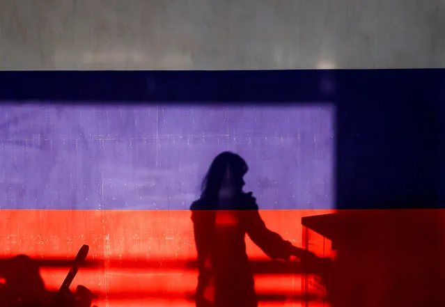 A woman is silhouetted behind a banner in the colours of the Russian flag at a polling station during the Russian presidential election in the settlement of Gorki Leninskie in the Moscow Region, Russia on March 15, 2024. (Photo by Maxim Shemetov/Reuters)