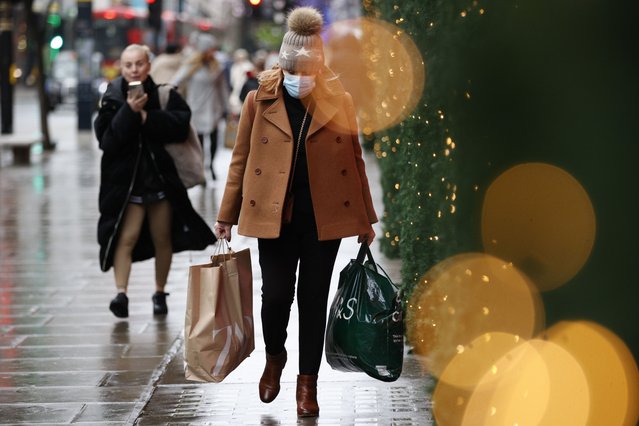 A woman wearing a face mask to guard against COVID-19 carries bags of shopping along Oxford Street in London, Monday, December 27, 2021. In Britain, where the omicron variant has been dominant for days, government requirements have been largely voluntary and milder than those on the continent, but the Conservative government said it could impose new restrictions after Christmas. (Photo by David Cliff/AP Photo)