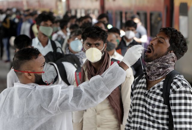A health worker collects a swab sample from a traveler at a train station to test for COVID-19 before allowing him to enter the city, in Mumbai, India, Wednesday, January 12, 2022. (Photo by Rajanish Kakade/AP Photo)