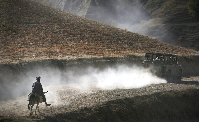 In this Tuesday, September 15, 2009 file photo made by Associated Press photographer Anja Niedringhaus, an Afghan man on his donkey follows a convoy of German ISAF soldiers patrolling Yaftal E Sofla, in the mountainous region of Feyzabad, east of Kunduz, Afghanistan. (Photo by Anja Niedringhaus/AP Photo)